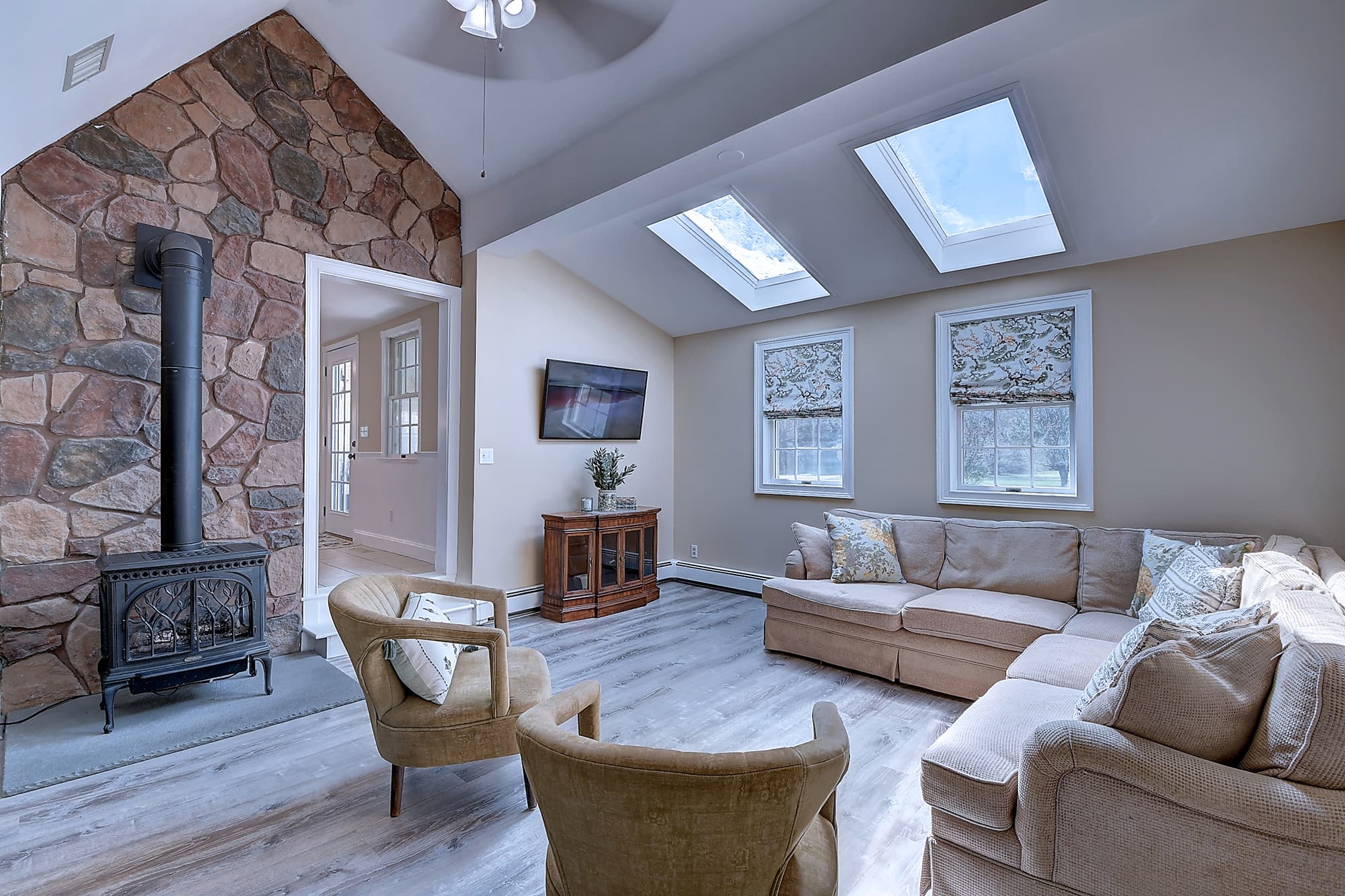 Family room with stone wood-stove fireplace, vaulted ceiling, and skylights