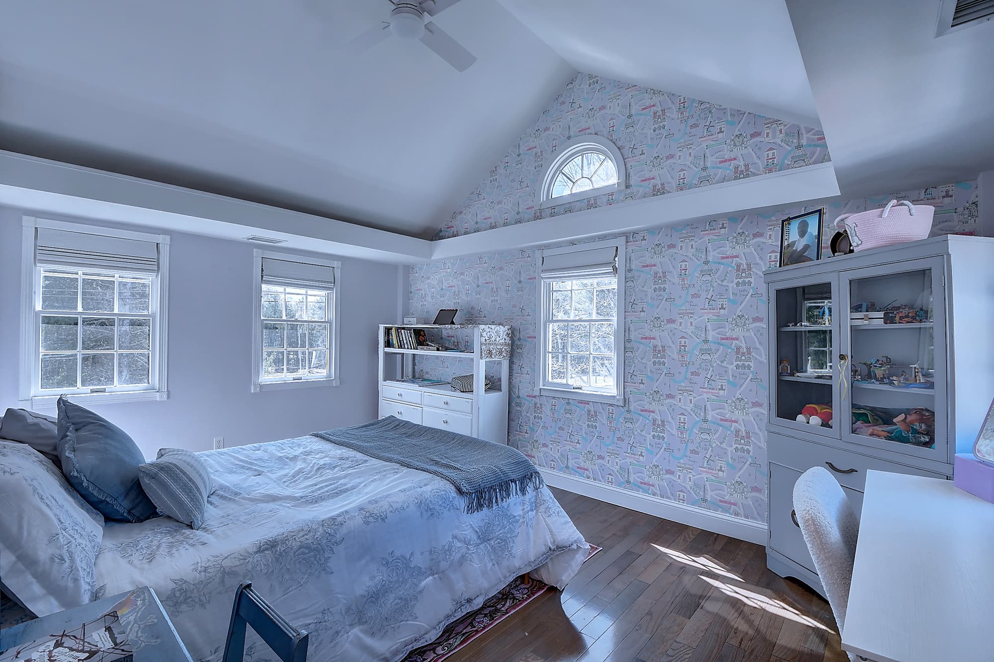 Vaulted-ceiling bedroom with arched window detail, hardwood flooring, and built-in storage
